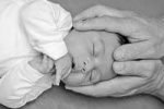 tête de bébé entourée par les mains du chiro